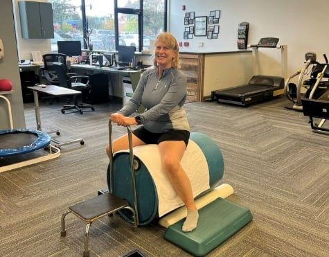 Mary Kent smiling for a photo as she mounts a piece of exercise equipment to rehabilitate her knee.