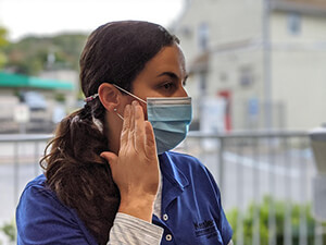 Female nurse in blue scrubs wearing blue medical mask.