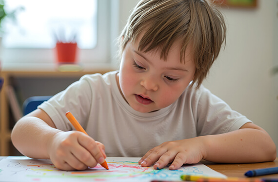 A young boy is sitting at a desk and coloring with crayons